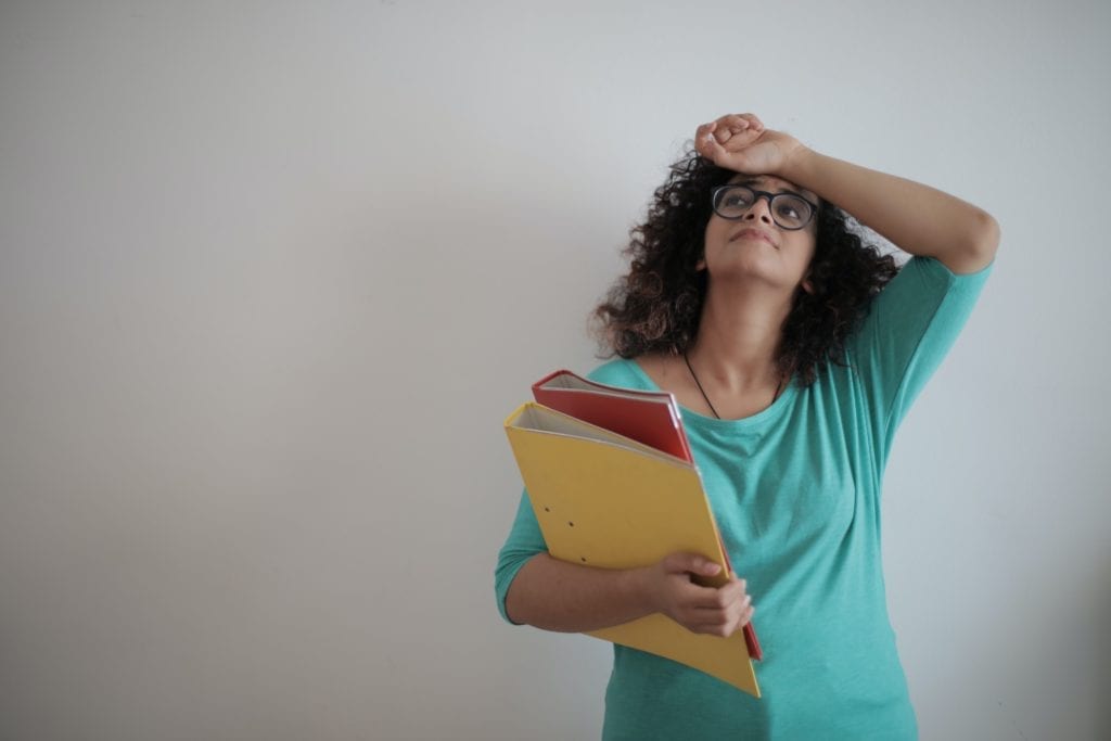 person holding two binders looking up with a hand across their forehead, palm up.
