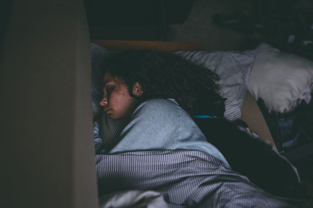 person laying on their bed in a dark room covered with a blanket