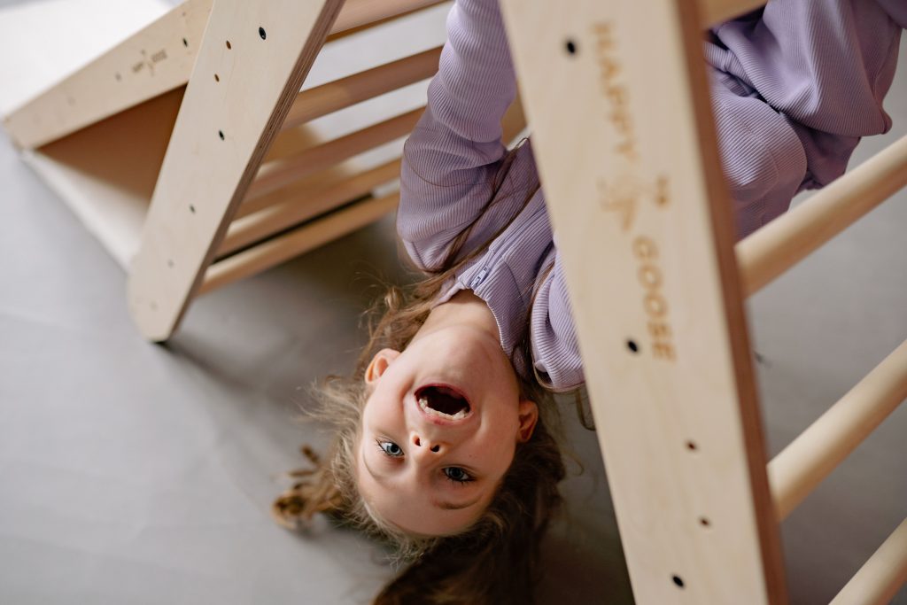 A child hanging upside down on play equipment. An example of a sensory seeker.