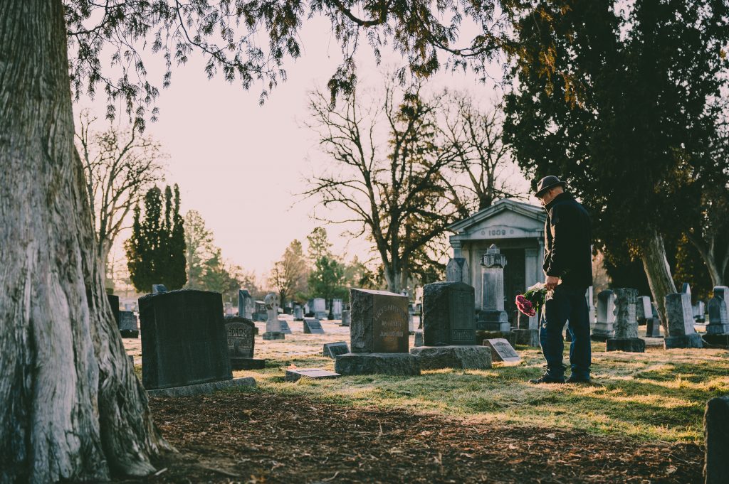 A person stands in front of a grave holding a bouquet of flowers.
