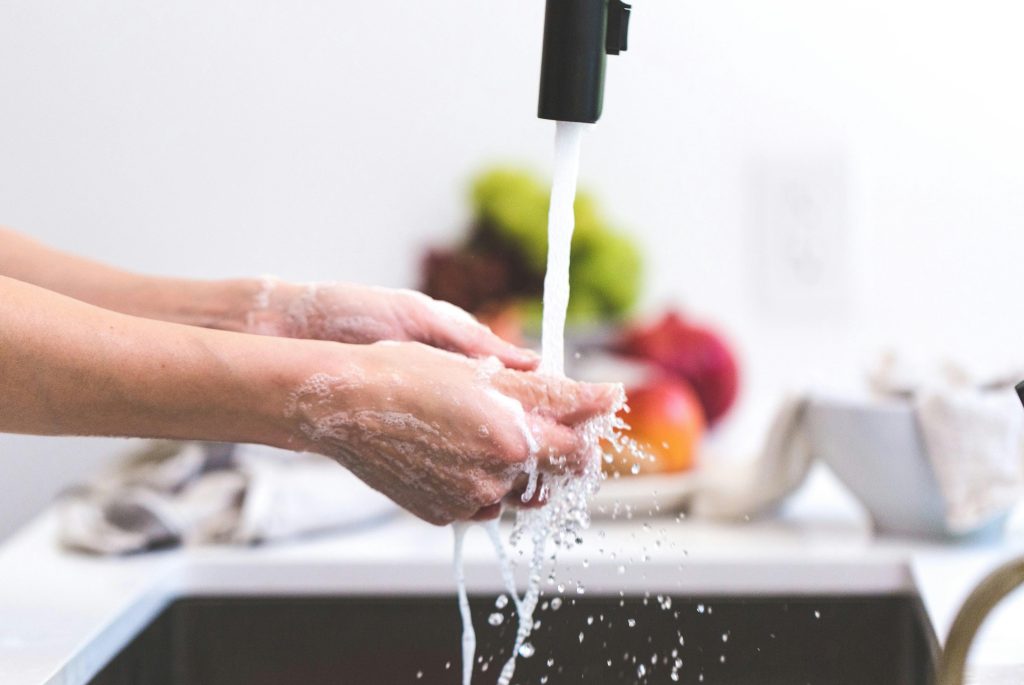 Person holding their hands under running water from the kitchen tap.