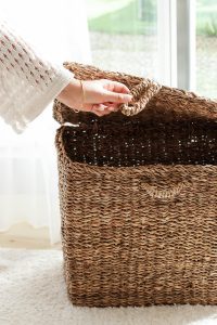 A person's hand reaching out to hold the lid open on a wicker basket.