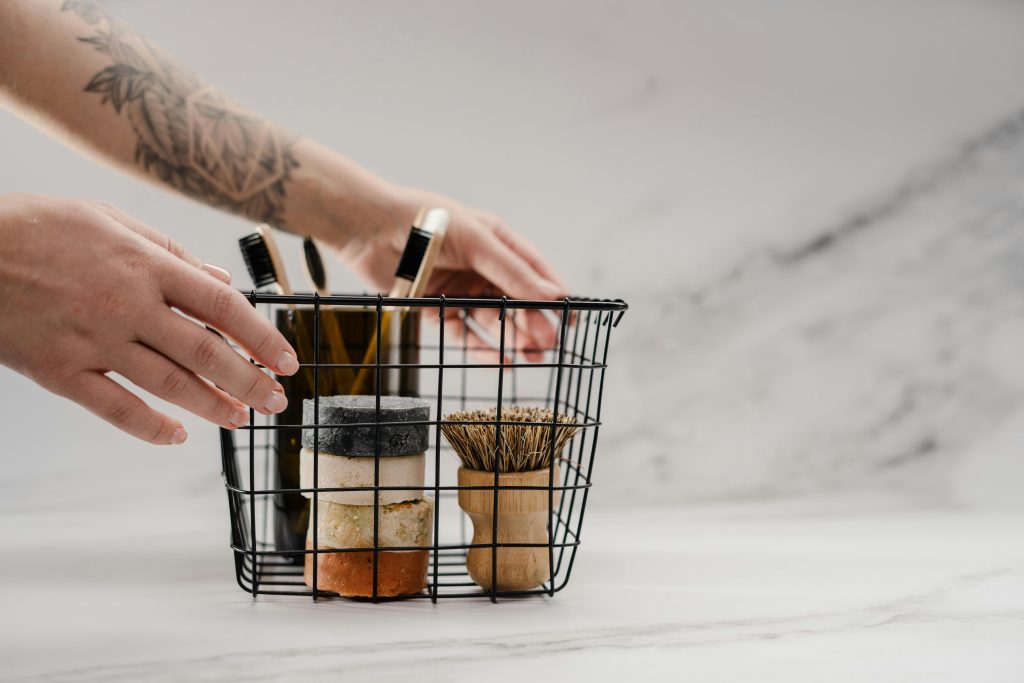 A person's hands are touching a wire basket full of bathroom toiletries.