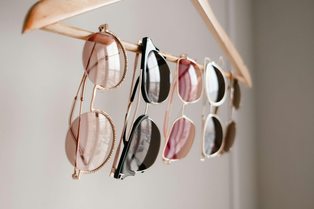 5 pairs of differently colored tinted glasses hanging on a clothes hangers.